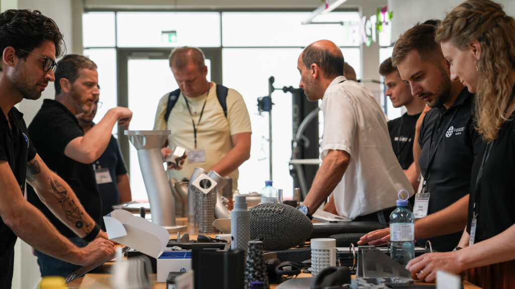 Personen stehen rund um einen Tisch auf dem 3D-Druckteile liegen
