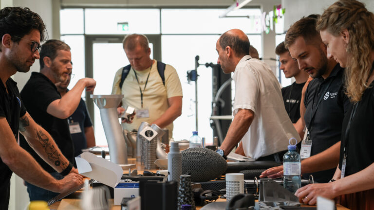 Personen stehen rund um einen Tisch auf dem 3D-Druckteile liegen